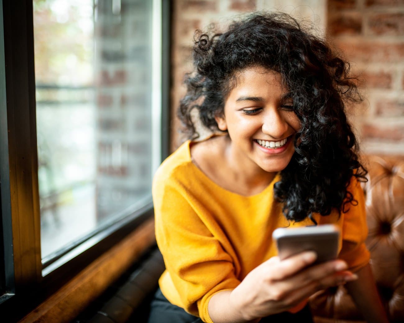 A woman smiling at her phone in a warm-lit café after redeeming her Visa gift card