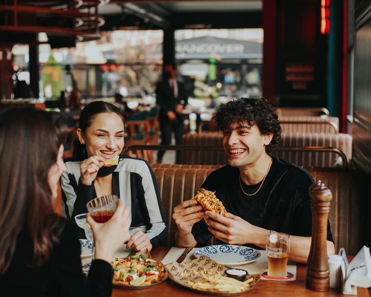 Three friends laughing together over food at a neighborhood restaurant