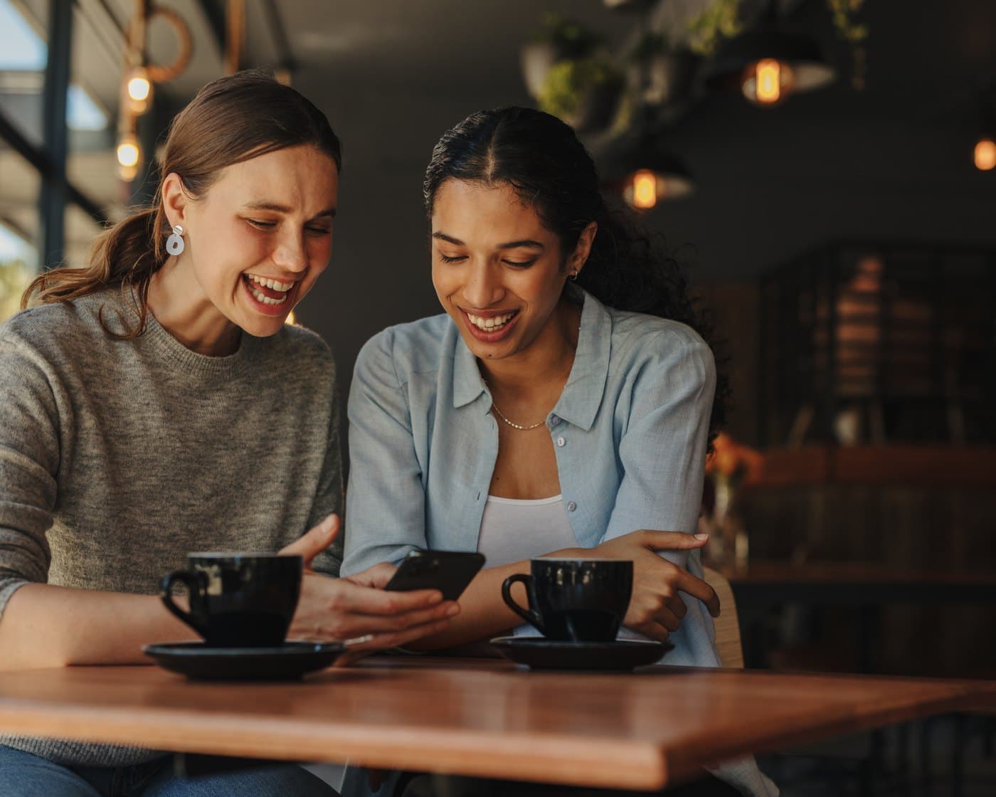 Two friends laughing together over a phone at a neighborhood café